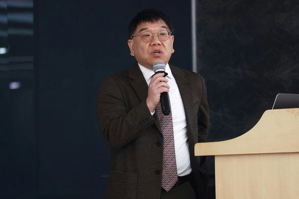 people-Man Speaking at Podium-Man with Glasses-Holding Microphone-Dark Suit Jacket