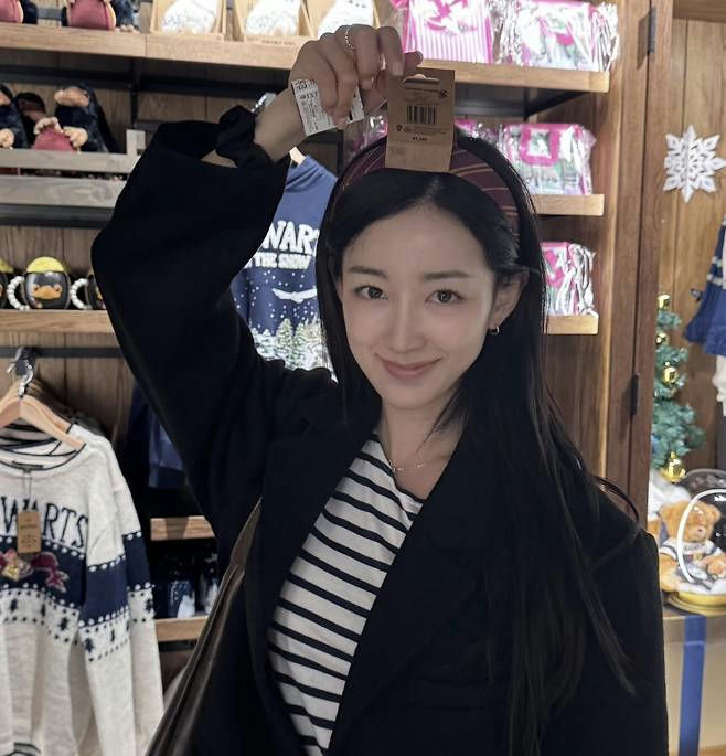 people-Chinese actress Jiang Shuying-smiling-holding up merchandise tag-wearing striped shirt and black blazer-in a store with merchandise visible