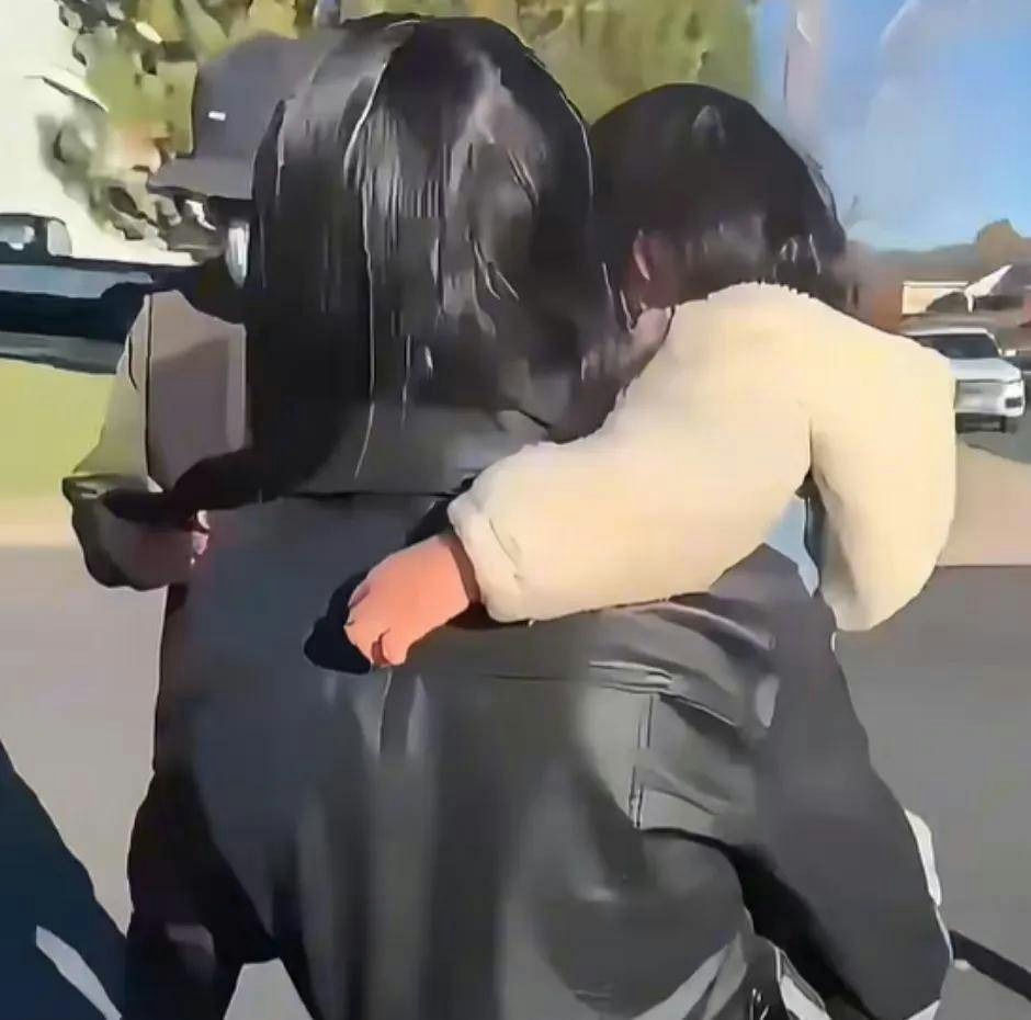 people-Person hugging child-Person in black leather jacket and cap-Child in cream/white jacket-Outdoor street scene