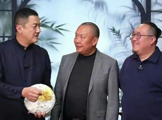 people-Man on left holding tea cake-Man in center in grey suit-Man on right wearing glasses-Smiling-Bamboo backdrop