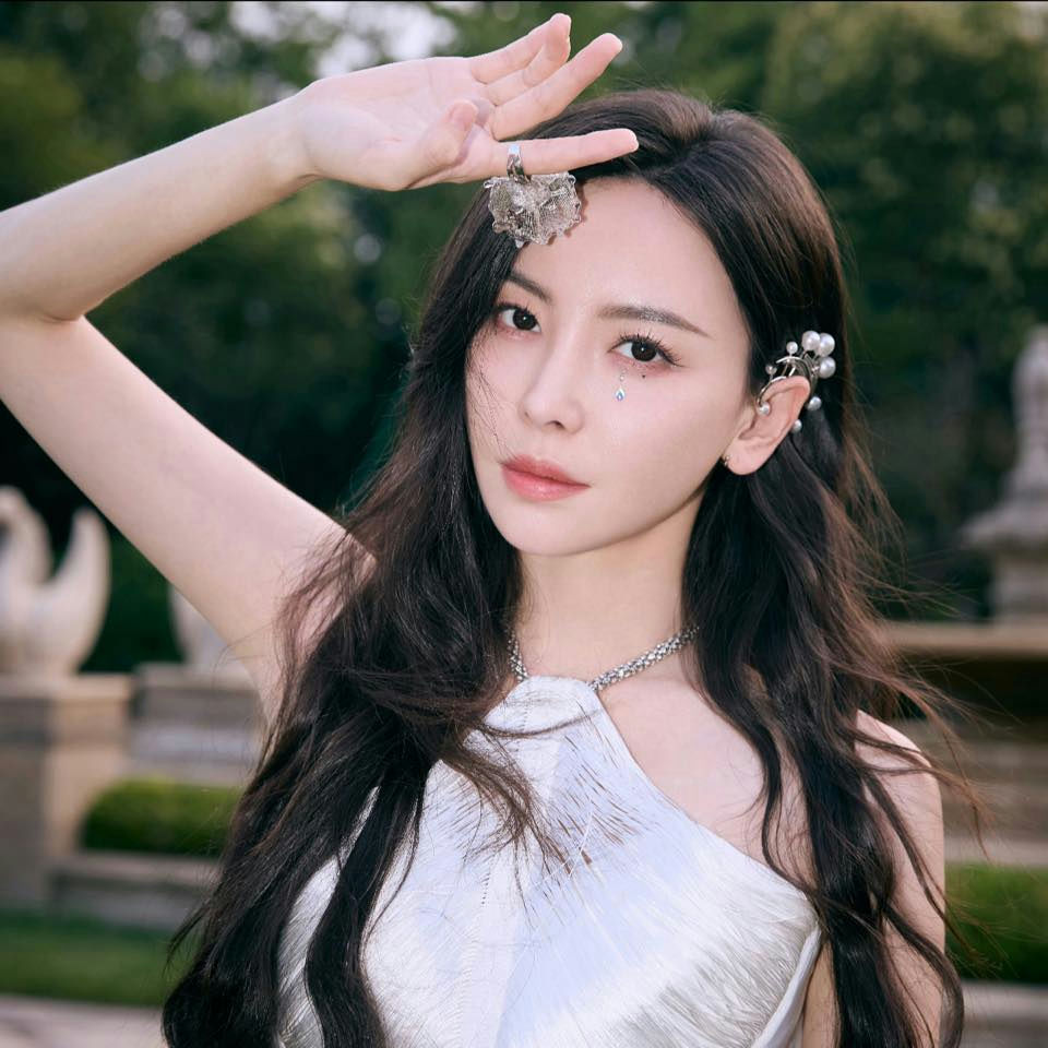 people-Zhang Yuqi-A-long dark wavy hair-A-silver halter top-B-crystal teardrop makeup accent-C-hand raised near forehead