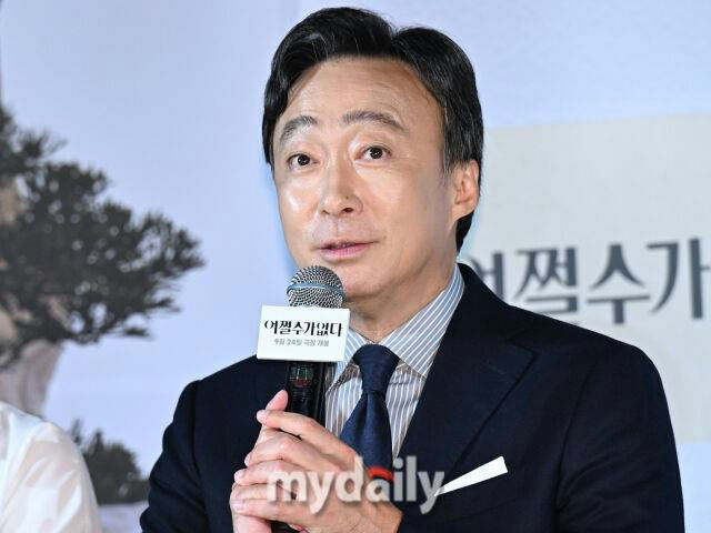 people-Actor Song Kang-ho-speaking at an event-holding a microphone-wearing a suit-Korean text visible on microphone flag