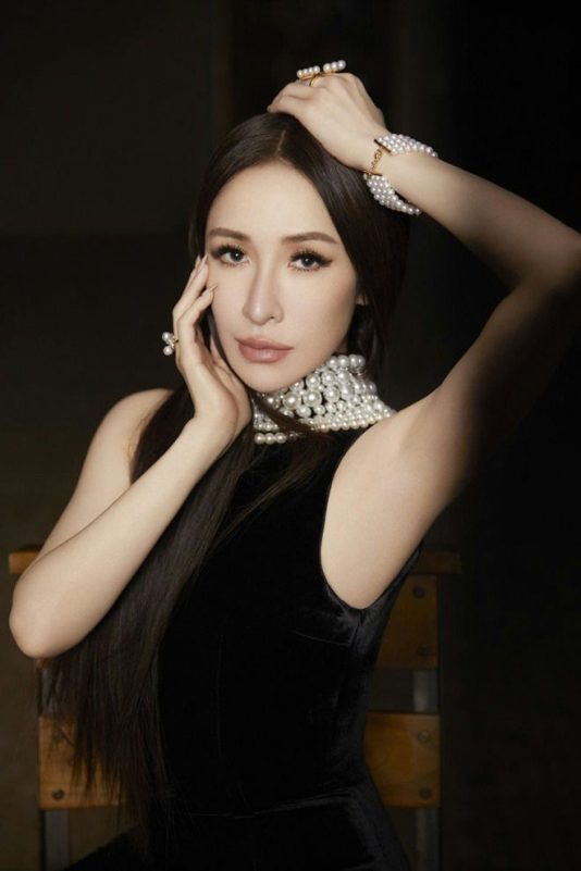 people-Taiwanese singer and actress Shu Qi-black velvet sleeveless dress-multi-layered pearl choker necklace-long straight dark hair-elegant pose with hands near face and head