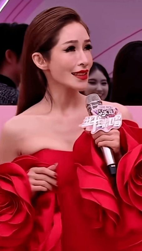 people-Taiwanese celebrity, host, and model Shu Qi (林立慧)-stunning red strapless gown with rose-like ruffles-holding a microphone with Chinese text logo-glamorous makeup with dramatic winged eyeliner and red lipstick