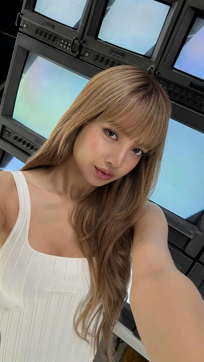 people-Lisa from BLACKPINK-A-selfie-A-long brown hair-B-bangs-B-white ribbed tank top-C-video monitors in background-C
