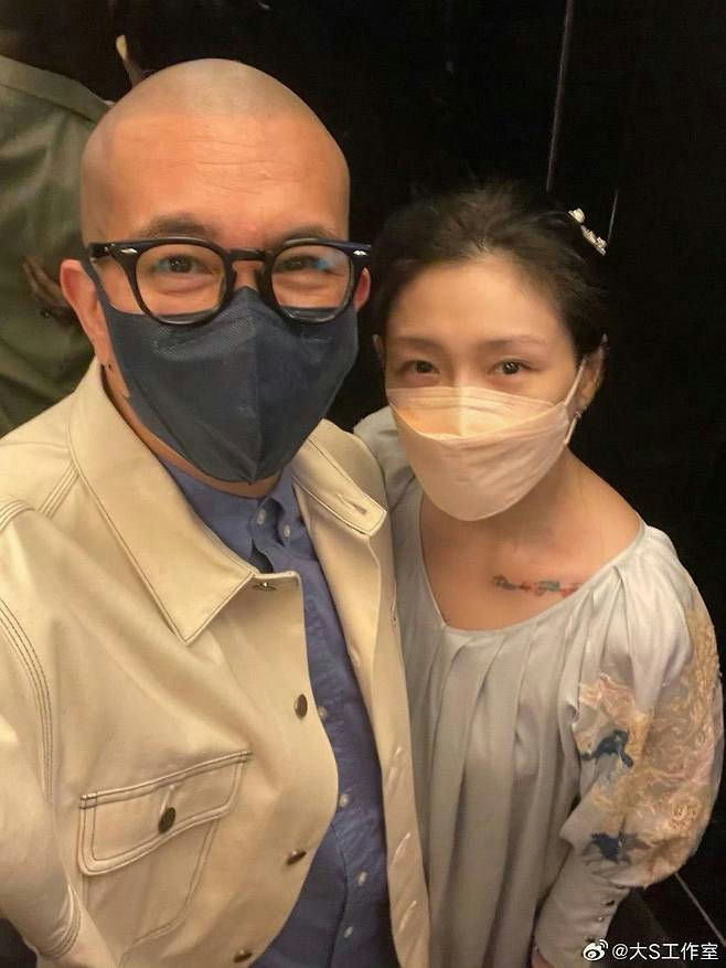 people-Barbie Hsu (Da S)-bald man wearing glasses and a mask-woman wearing a light pink mask and a light blue top-selfie-tattoo on collarbone