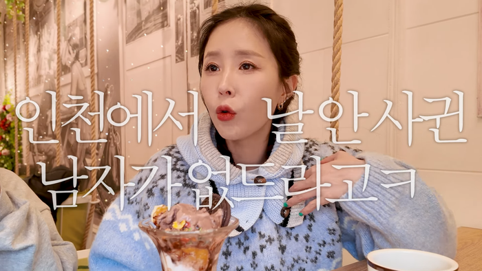 people-Korean female vlogger-a woman eating a dessert-a woman wearing a patterned blue and white sweater-text overlays in Korean