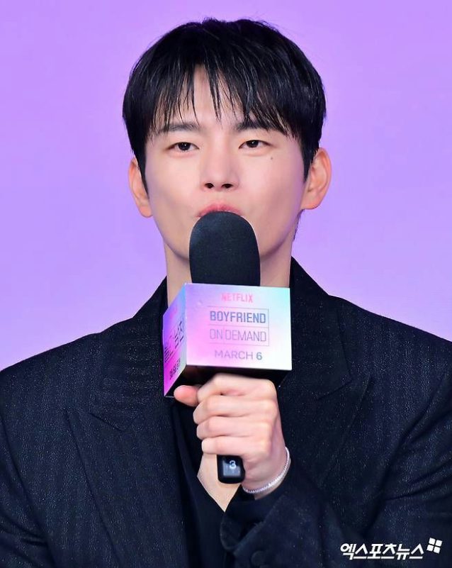 people-Lee Je-hoon-speaking into a microphone-at a press event-wearing a black suit-with a light purple background