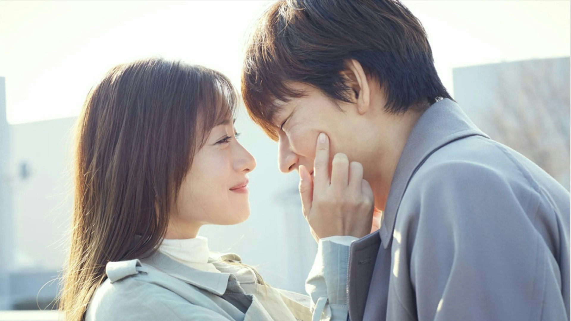 people-Two East Asian individuals-A-intimate moment-A-man touching woman's cheek-B-soft lighting-B-romantic-C-outerwear-C-light gray coat