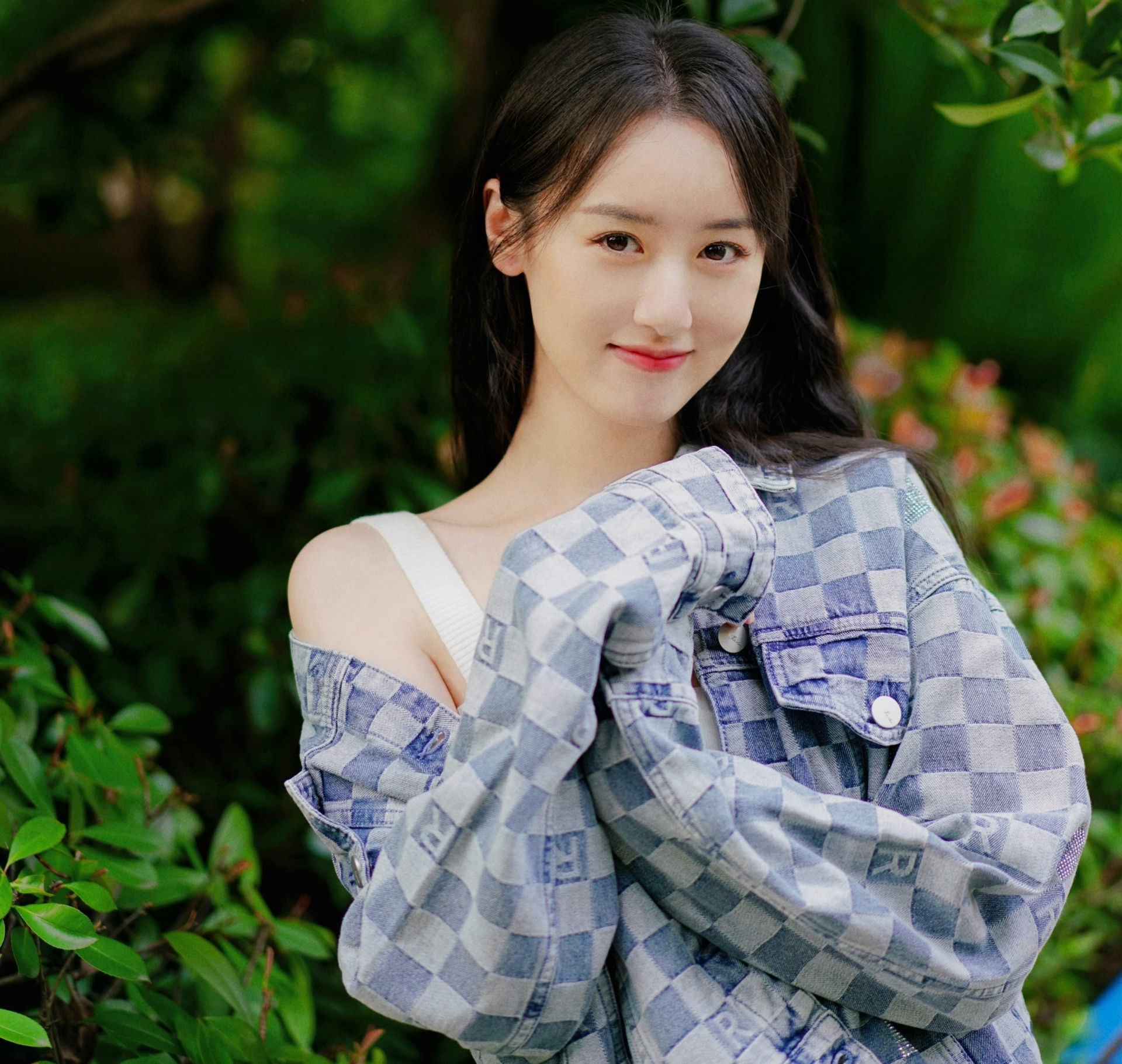people-Zhao Lusi-outdoor portrait-smiling-wearing checkered denim jacket-long black hair-lush green background