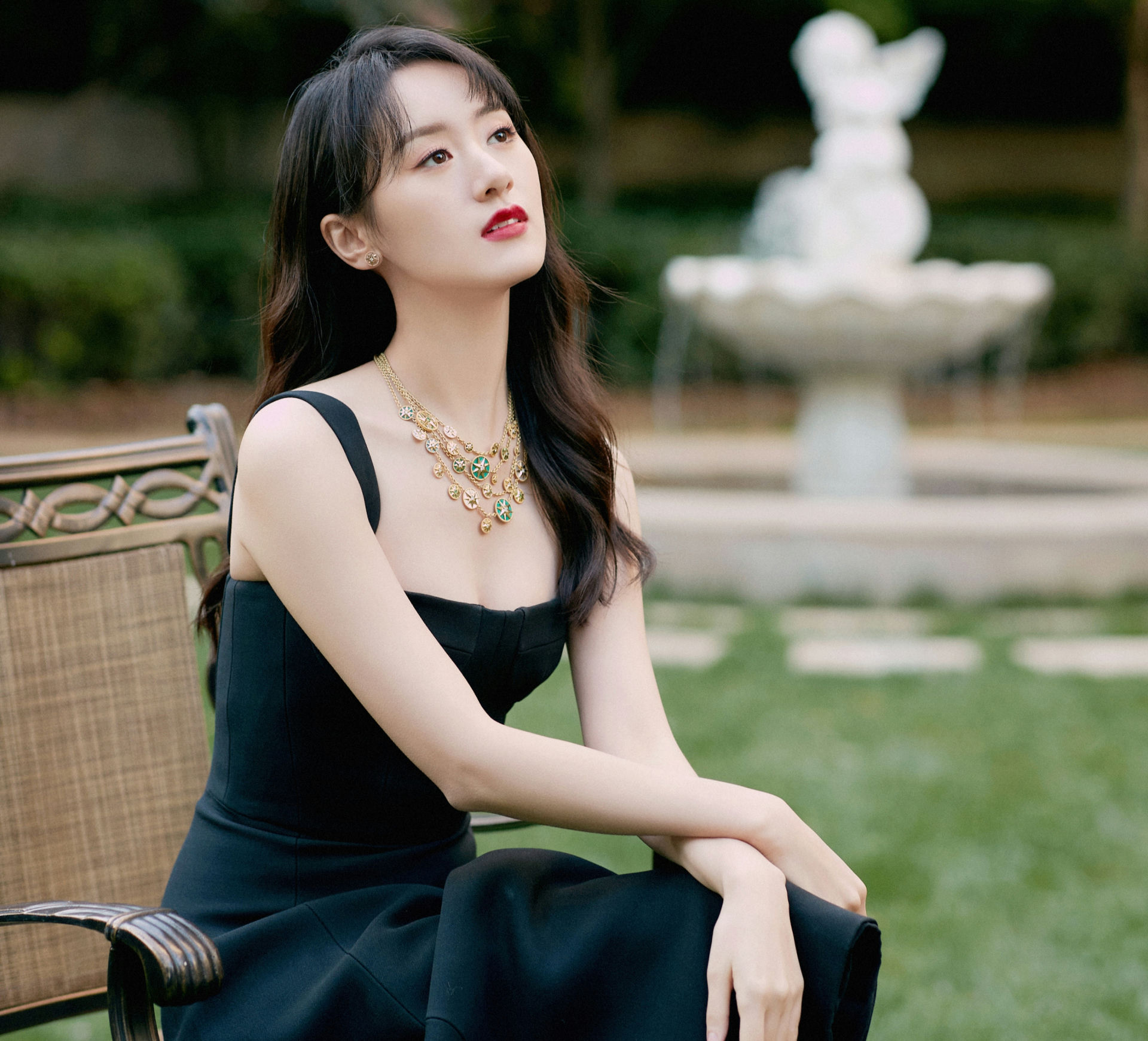 people-Zhang Jingyi-sitting outdoors-A-black dress-A-gold and green necklace-B-looking up-C-garden setting