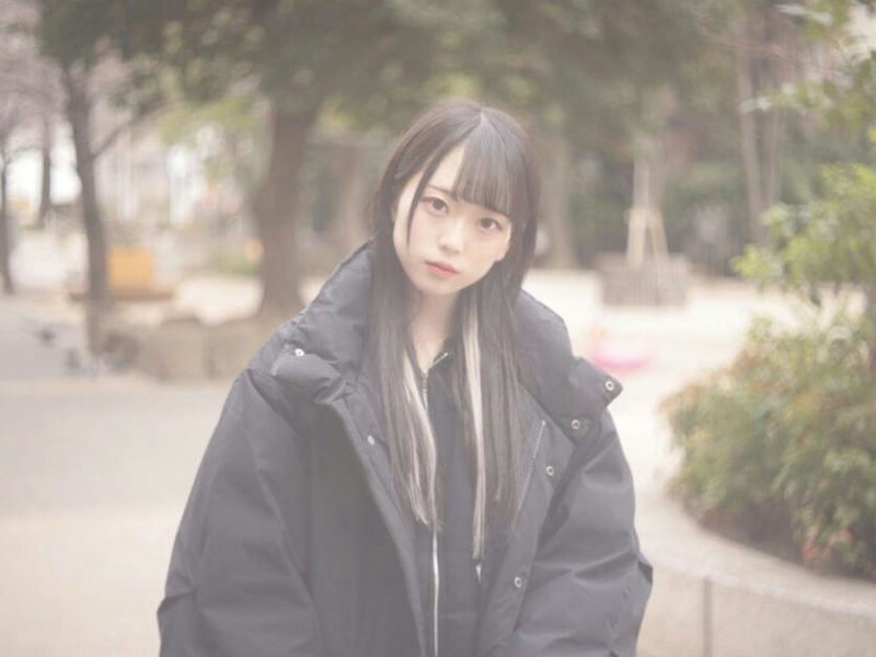 people-Young East Asian woman-A-long dark hair with light streaks-A-wearing a black puffer jacket-B-outdoors in a park-like setting-C-soft, slightly washed-out lighting