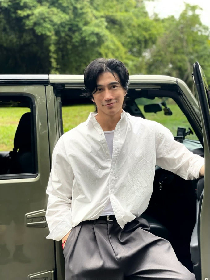 people-Godfrey Gao-standing outdoors by a car-white collared shirt-dark wide-leg trousers-black hair-smiling