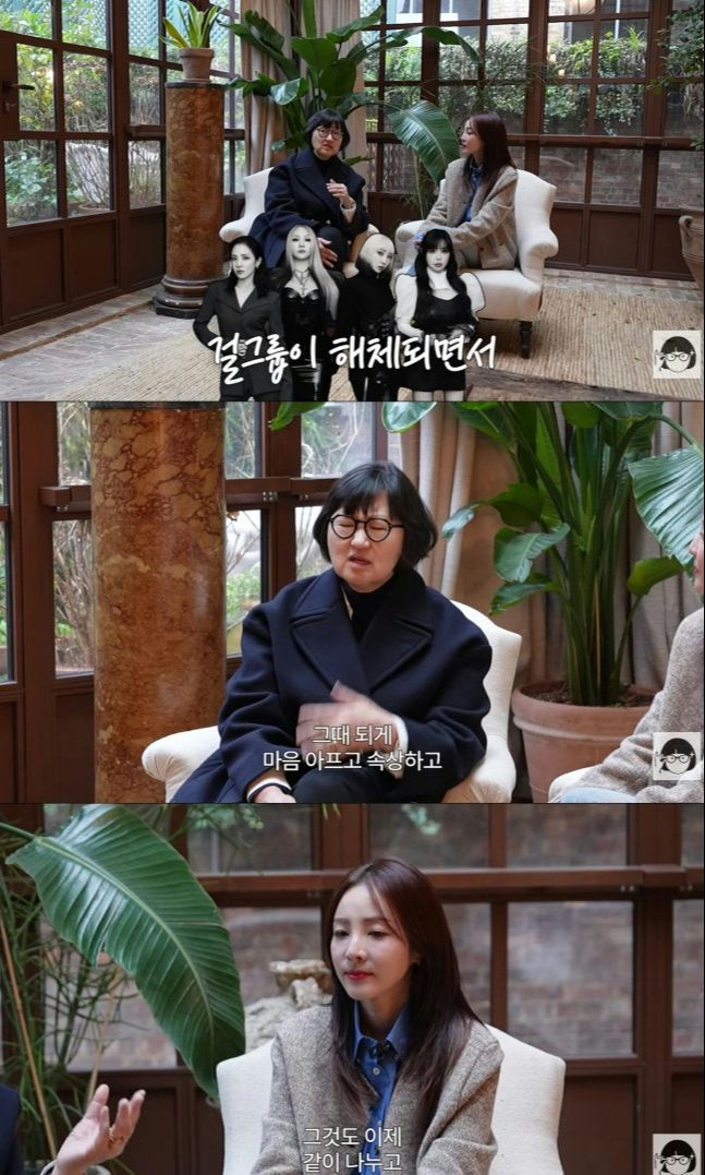 people-woman in dark coat speaking-woman in tweed jacket listening-four women in black outfits superimposed-Korean text-sadness-interview-A-dark interior with plants-A-formal seating arrangement-A-TV show screenshot-B-sadness-B-interview subject-B-Korean subtitles-C-Korean celebrity-C-YG Entertainment producer-C-2NE1 members
