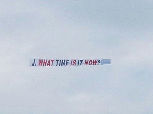 people-No people visible-A-Airplane banner-A-Message "J. WHAT TIME IS IT NOW?"-B-Sky-C-Outdoors