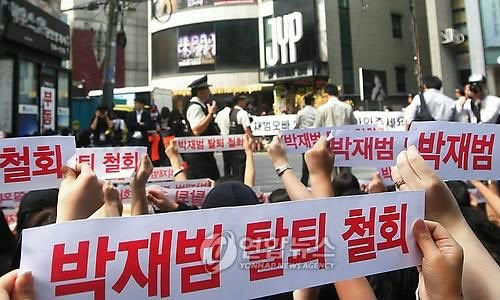 people-protestors-A-holding signs-A-in front of JYP Entertainment building-B-police officers present-C