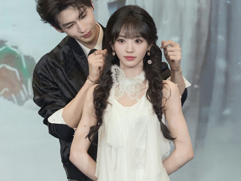 people-Chen Feiyu and Zhou Ye-posing for photo-black bomber jacket-white layered dress-braided pigtails-male leaning over female