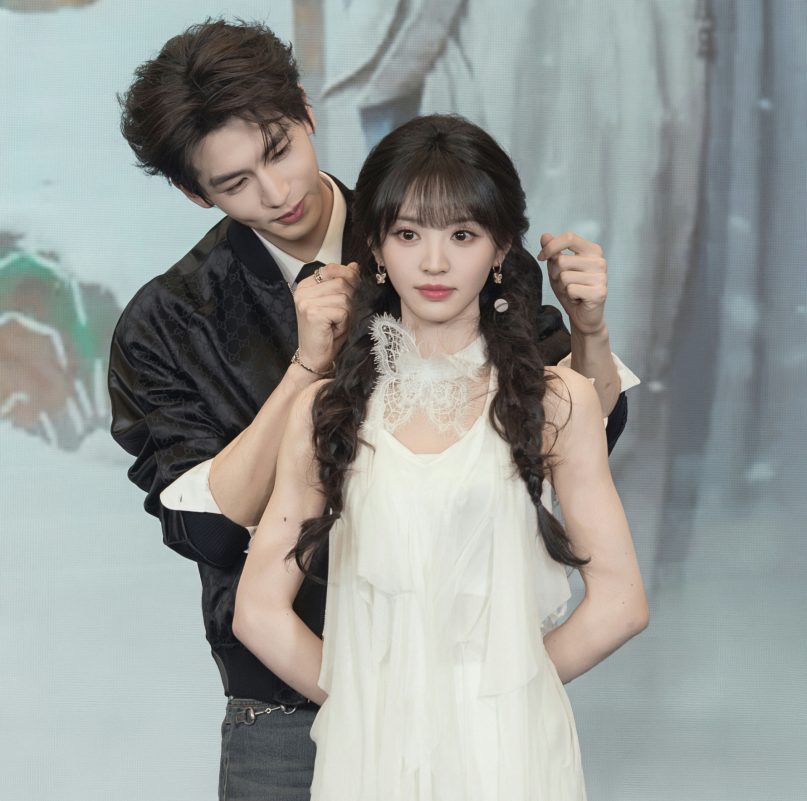 people-Chen Feiyu and Zhou Ye-posing for photo-black bomber jacket-white layered dress-braided pigtails-male leaning over female