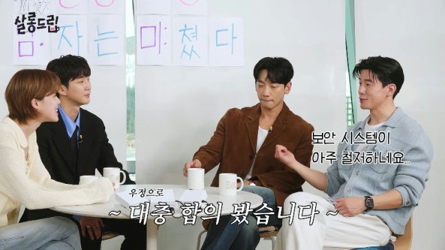 people-Rain-Ji-Hoon-in-brown-jacket-and-white-t-shirt-A-woman-with-short-brown-hair-in-a-cream-colored-sweater-A-man-in-a-black-suit-and-blue-shirt-A-man-in-a-light-blue-overshirt-A-casual-meeting-or-talk-show-setting-with-Korean-text-on-the-wall-and-subtitles-A-white-table-with-mugs-in-front-of-the-people-A-casual-and-engaged-atmosphere