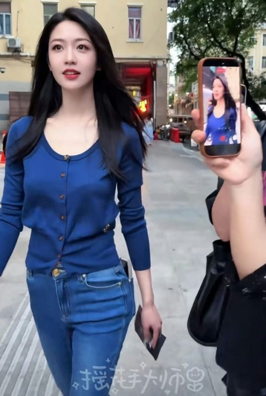 people-Woman in blue cardigan and jeans-Street setting-Filming with smartphone-Long dark hair