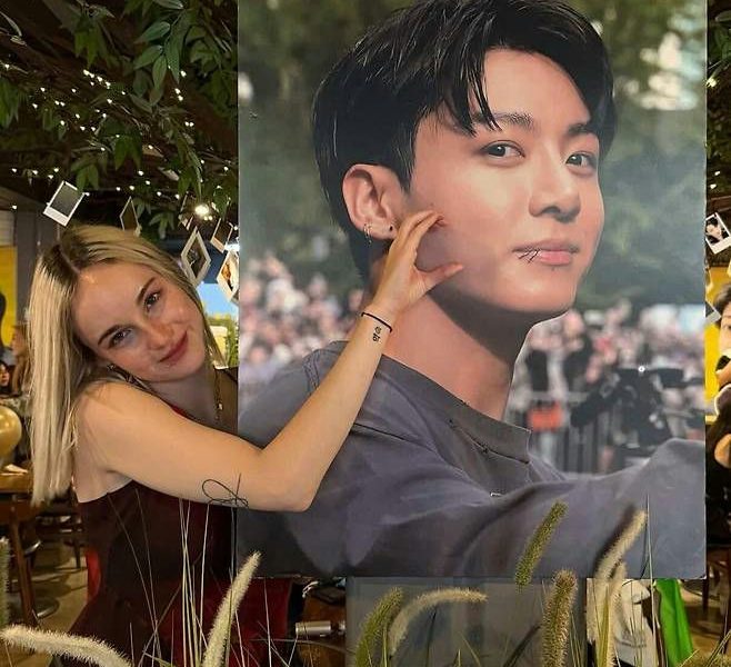 people-Woman hugging poster-Poster of Jungkook-Jungkook's face-Woman's arm touching poster