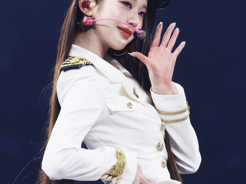people-IVE Jang Wonyoung-Kpop idol-A-white naval uniform-A-long brown hair-A-performing on stage-A-hand raised in wave-A-baseball cap style hat