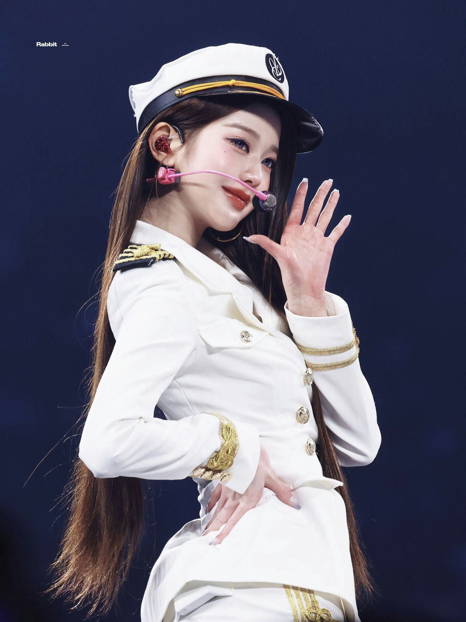 people-IVE Jang Wonyoung-Kpop idol-A-white naval uniform-A-long brown hair-A-performing on stage-A-hand raised in wave-A-baseball cap style hat