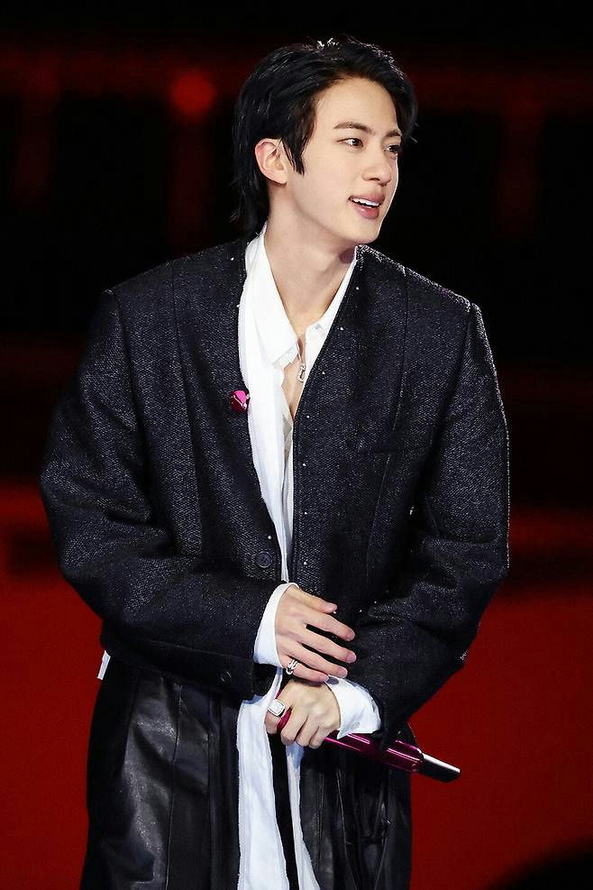 people-Jin (BTS)-performer-black textured cropped jacket-white unbuttoned shirt-holding pink microphone-red background