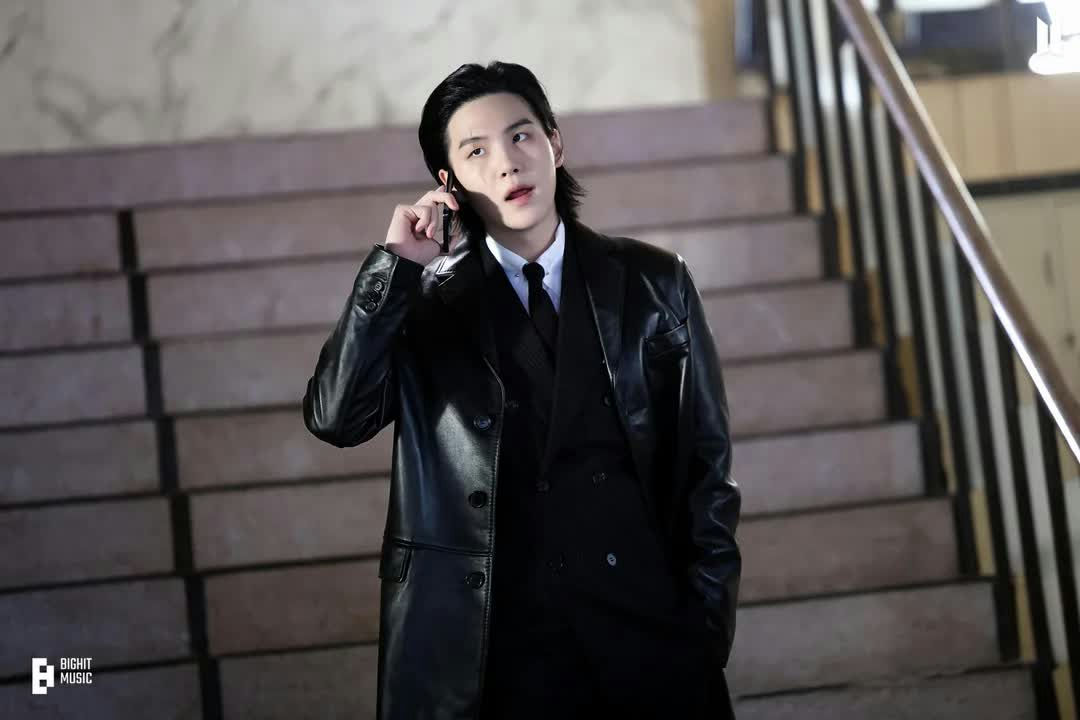 people-SUGA (BTS)-black leather trench coat-on phone-staircase background-serious expression